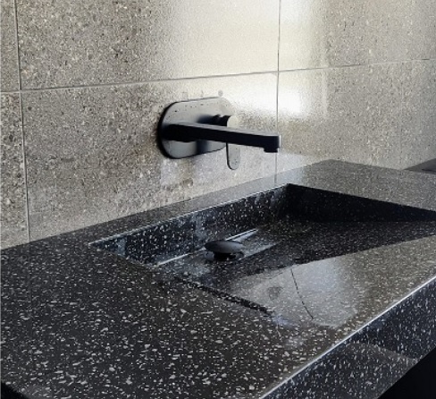 Modern black stone sink in newly renovated bathroom. Natural grey wall tiles fixed behind and above sink.